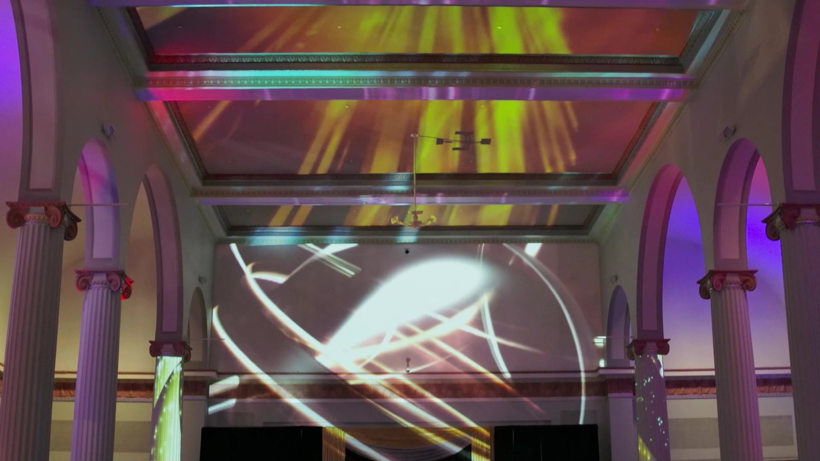 Yellow light rays mapped to the ceiling bays, white arcs on the back wall and green and blue textures on the columns at Historic Union Station