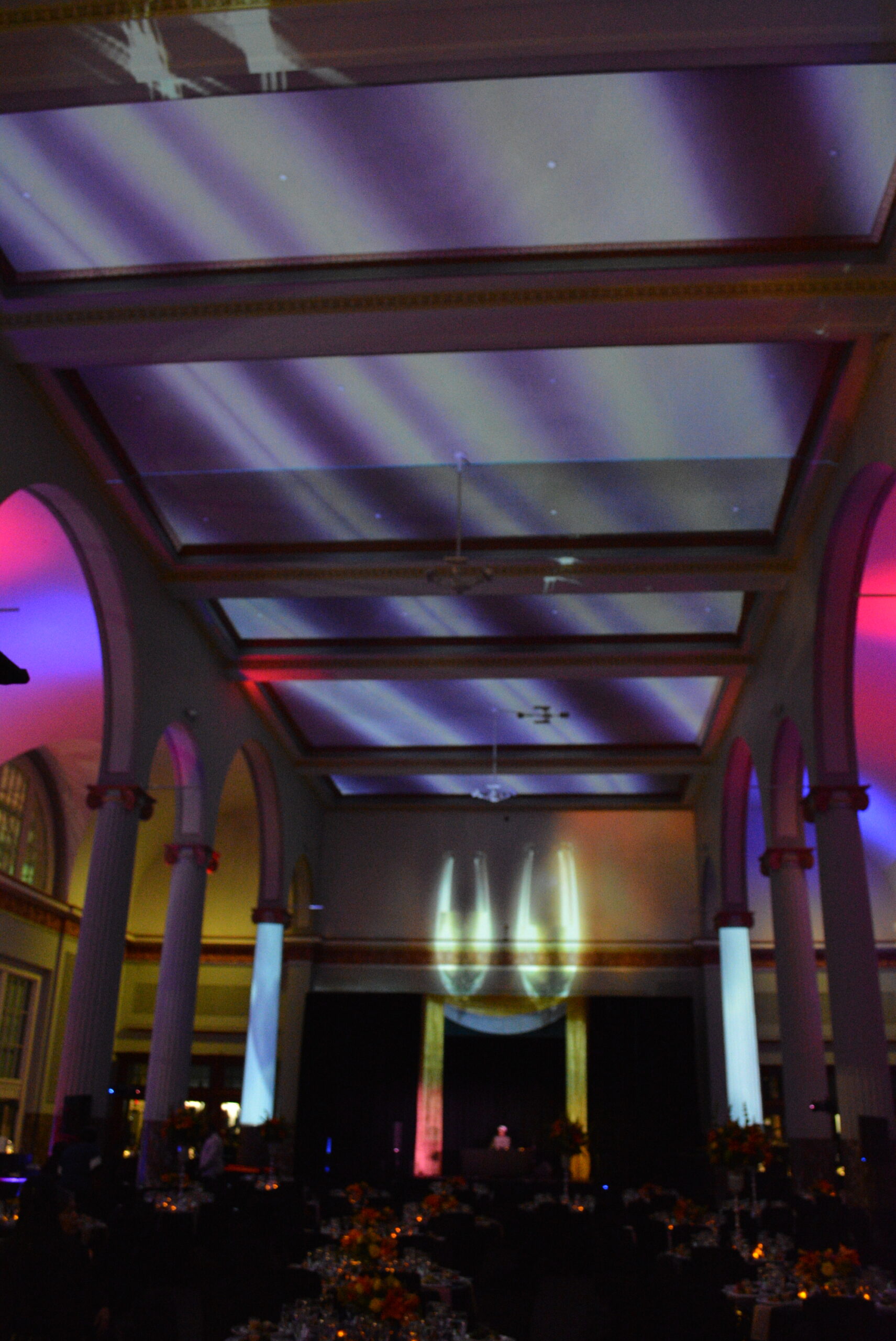 Projection-mapped light bands across the coffered ceiling and flame imagery on the back wall between uplit columns at Historic Union Station
