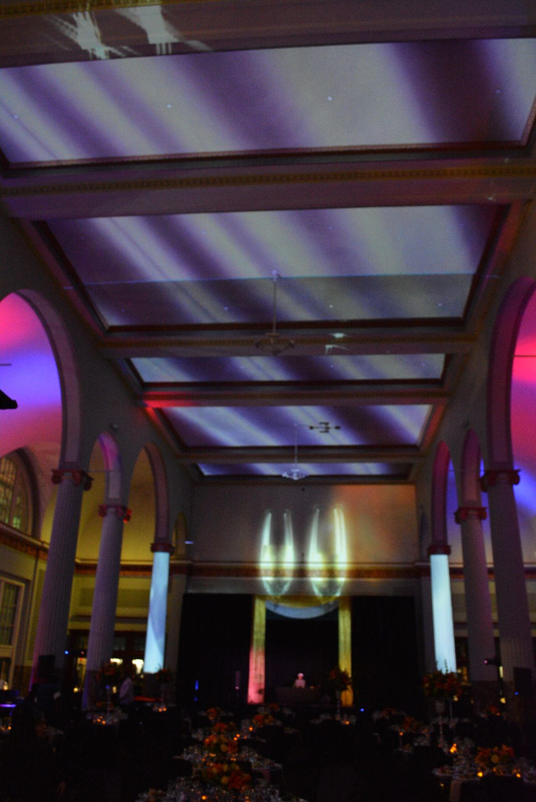 Projection-mapped light bands across the coffered ceiling and flame imagery on the back wall between uplit columns at Historic Union Station